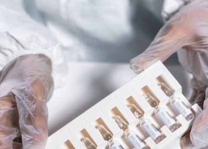 Healthcare worker in protective gear handling vials in a laboratory setting.