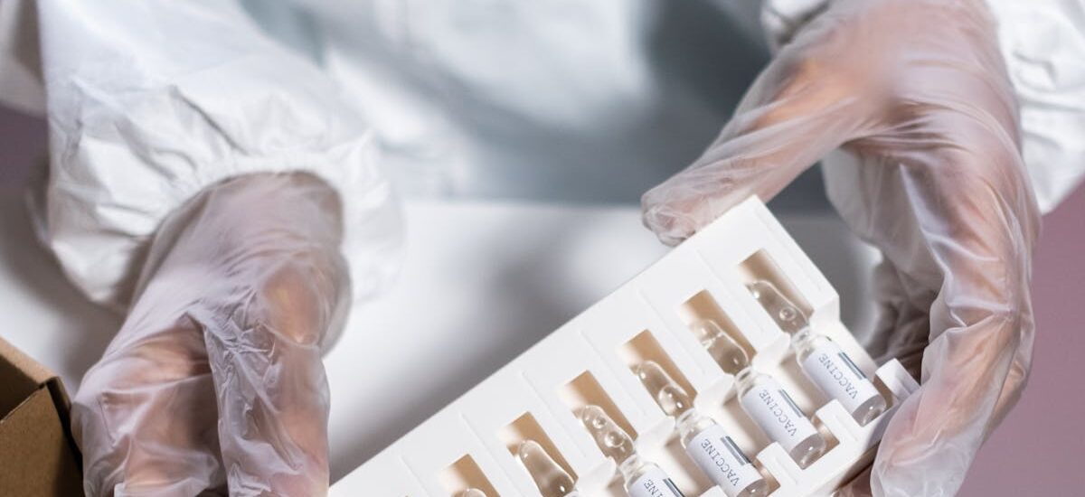 Healthcare worker in protective gear handling vials in a laboratory setting.