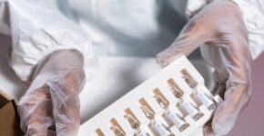 Healthcare worker in protective gear handling vials in a laboratory setting.