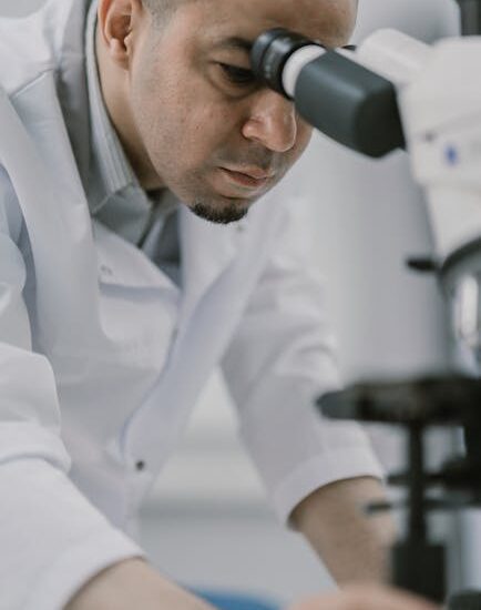 Scientist in laboratory observing a sample through a microscope with focus and precision.