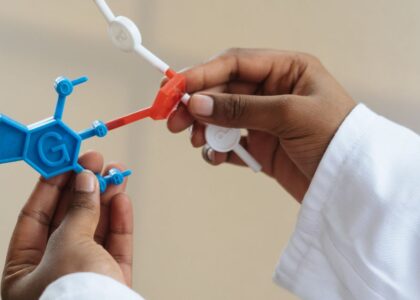 Unrecognizable ethnic scientist wearing lab coat and examining plastic molecule model while standing in laboratory after necessary research