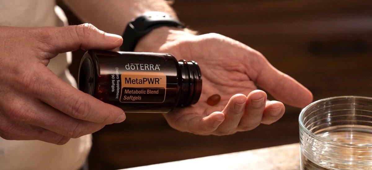 Hand holding MetaPWR metabolic blend softgels next to a glass of water.