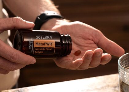 Hand holding MetaPWR metabolic blend softgels next to a glass of water.